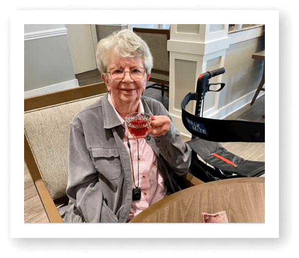 Elderly Woman Holding Drink and Smiling at Table at Assisted Living Facility