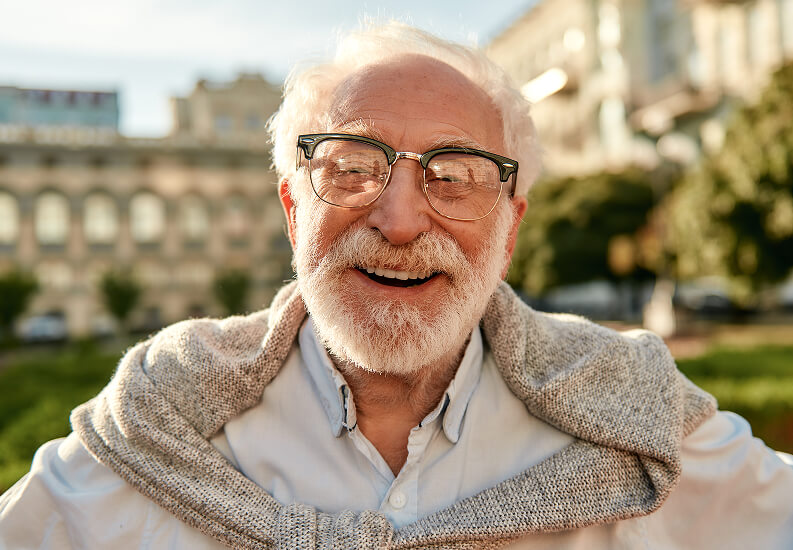 Elderly Man with Glasses Smiling Outdoors Wearing Scarf at Assisted Living Facility Elderly Man with Glasses Smiling Outdoors Wearing Scarf at Assisted Living Facility